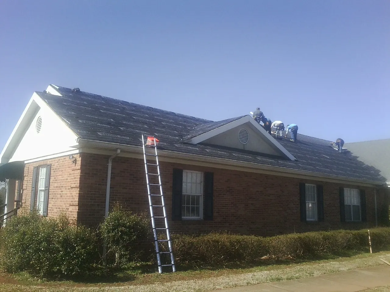 Crew tearing shingles off a brick ranch roof with a ladder set — Emergency Roof Repair work by our crew in Edinburgh