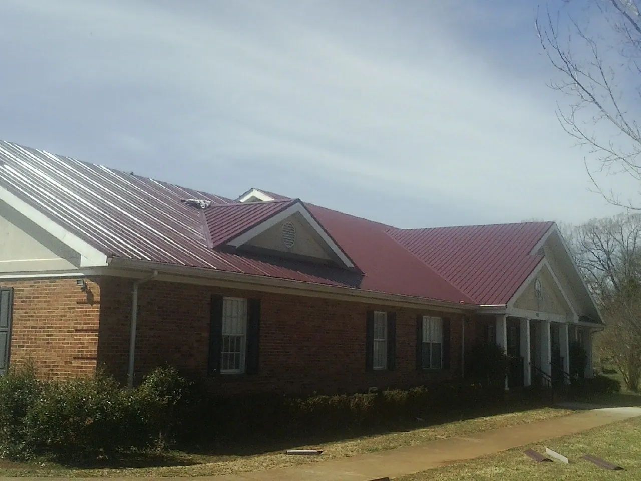 Red metal roof with gabled entries on a long brick building, from a Hail Damage Roof Repair job in Edinburgh