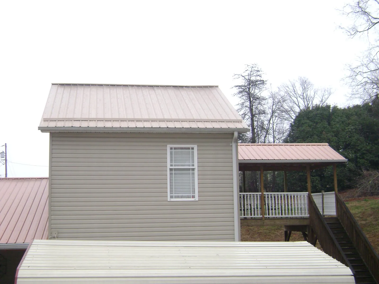 Tan metal roofs on a two story addition and attached porch, from a Roof Replacement job in Edinburgh